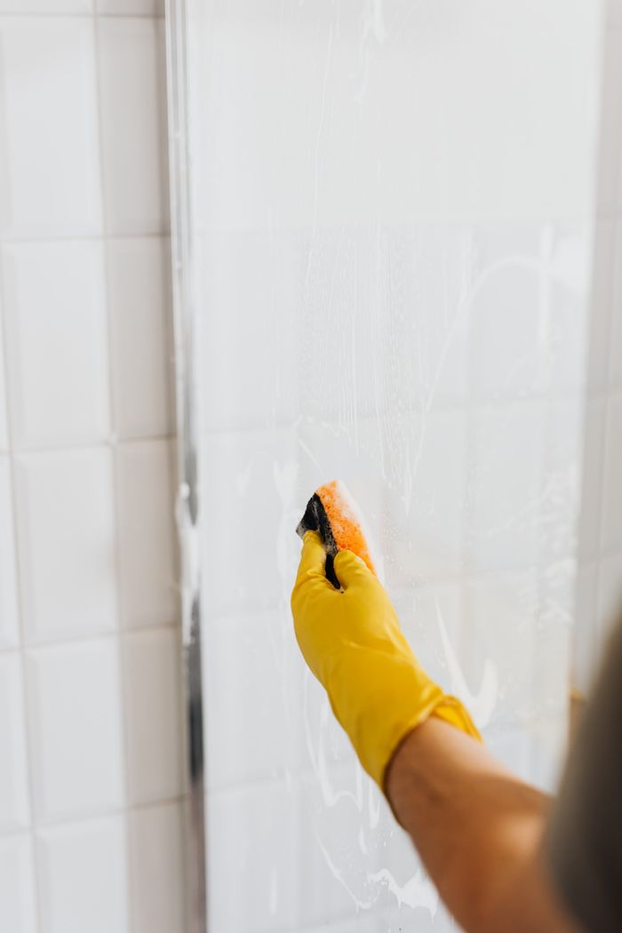 about-02 Crop faceless person in yellow rubber protective glove using detergent and sponge for cleaning walk in shower glass