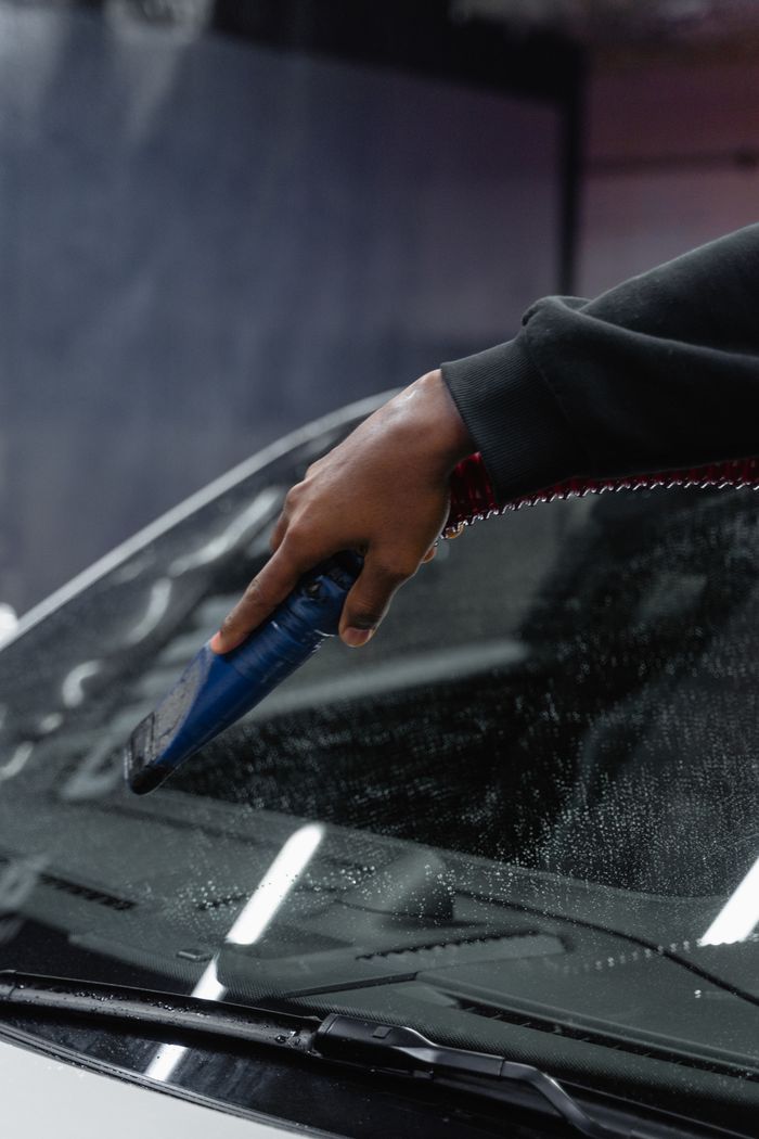 Close-up of a hand using a blower tool to dry a car windshield at an indoor carwash.