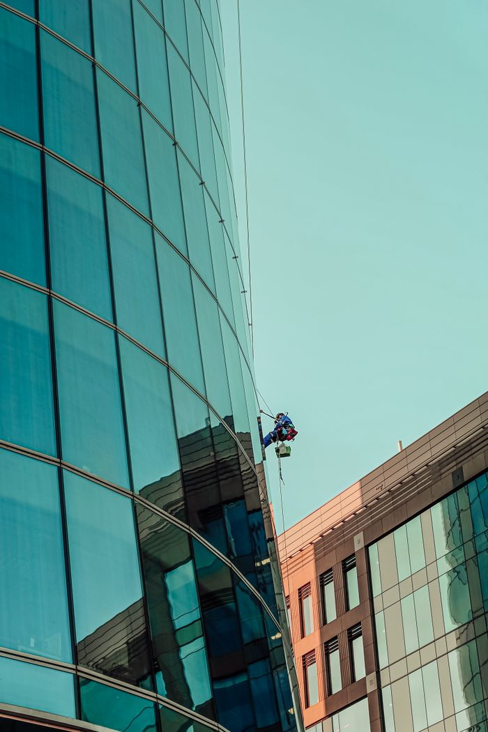 A professional window cleaner working on a tall modern building against a blue sky.